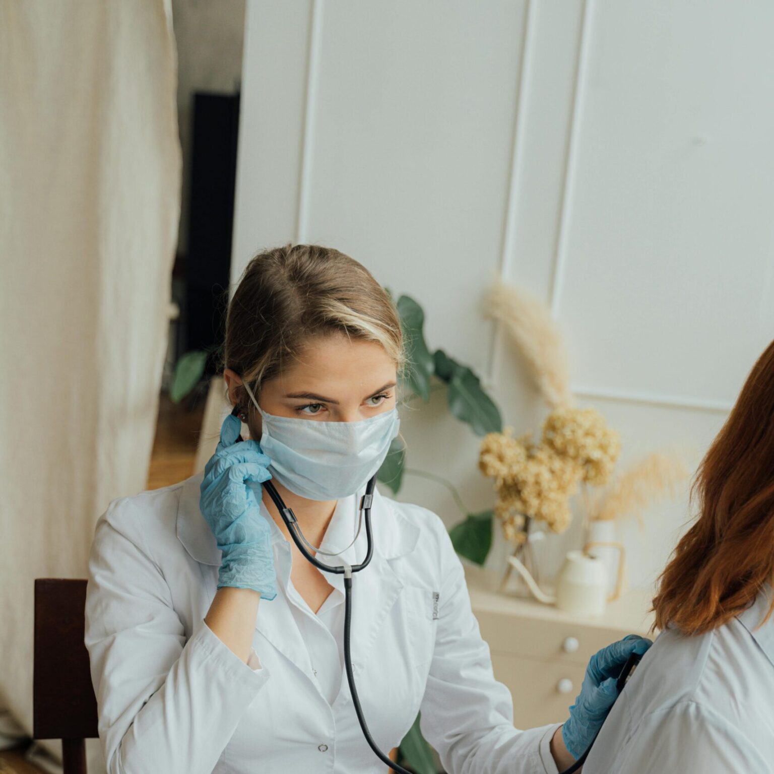 A healthcare professional in PPE using a stethoscope for a medical check-up.